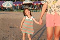 Happy little Asian child girl holding mother hands on beach while evening sunlight