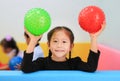 Happy little Asian child girl holding round silicone inflatable green and red knobby ball in children room