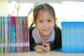 Happy little Asian child girl lying on bookshelf at library. Children creativity and imagination concept Royalty Free Stock Photo