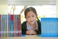 Happy little Asian child girl lying on bookshelf at library. Children creativity and imagination concept Royalty Free Stock Photo