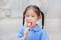Happy little Asian child girl in school uniform enjoy eating sausage outdoors