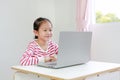 Happy little asian child girl sitting at desk and using laptop computer stay at home Royalty Free Stock Photo