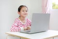 Happy little asian child girl sitting at desk and using laptop computer stay at home Royalty Free Stock Photo