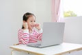 Happy little Asian child girl sitting at desk and using laptop computer stay at home Royalty Free Stock Photo