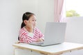 Happy little asian child girl sitting at desk and using laptop computer stay at home Royalty Free Stock Photo