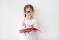 Happy little Asian child girl wearing eyeglasses and hold a book and write with pencil on white background Royalty Free Stock Photo