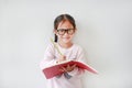 Happy little Asian child girl wearing eyeglasses and hold a book and write with pencil on white background Royalty Free Stock Photo