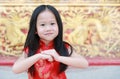 Happy little Asian child girl wearing red cheongsam with greeting gesture celebration for Chinese New Year at chinese temple in Royalty Free Stock Photo