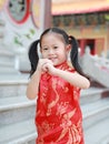 Happy little Asian child girl wearing red cheongsam with greeting gesture celebration for Chinese New Year at chinese temple in Royalty Free Stock Photo