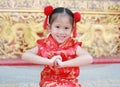 Happy little Asian child girl wearing red cheongsam with greeting gesture celebration for Chinese New Year at chinese temple in Royalty Free Stock Photo