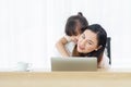 Happy little Asian daughter and mother using computer laptop, have a cheerful expression in the house