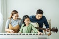 Happy little Asian daughter playing piano with mother and father play guitar at home, Mother teaching daughter to play piano, Royalty Free Stock Photo