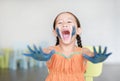 Happy little Asian girl with her blue hands and cheek painted in the children room Royalty Free Stock Photo