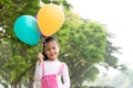 Happy little asian girl playing colorful balloons outdoors. Trees and green gardens background. Smiling lovely girl with balloons Royalty Free Stock Photo