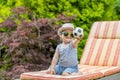 Happy little baby boy is sitting on the deck chair and showing little soccer balloon toy Royalty Free Stock Photo