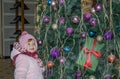 Happy little baby girl is beautiful in a white fur coat, hat, scarf near a Christmas tree decorated with toys and garlands and smi Royalty Free Stock Photo