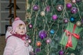 Happy little baby girl is beautiful in a white fur coat, hat, scarf near a Christmas tree decorated with toys and garlands and smi Royalty Free Stock Photo