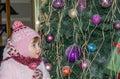 Happy little baby girl is beautiful in a white fur coat, hat, scarf near a Christmas tree decorated with toys and garlands and smi Royalty Free Stock Photo