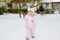 Happy little baby girl making first steps outdoors in winter through snow. Cute toddler learning walking. Child having Royalty Free Stock Photo