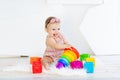 Happy little baby girl sitting in a white room in a red dress with bright toys