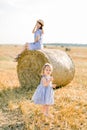 Happy little baby girl in wheat field with hay bales on warm and sunny summer evening, holding wheat spikelets, while Royalty Free Stock Photo