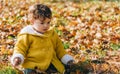 Happy little baby girl in yellow jacket playing with autumn leaves in park. Child smiling having fun in forest and exploring the Royalty Free Stock Photo