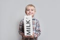 Happy little blond boy is holding a big white carton milk package. Light background Royalty Free Stock Photo