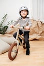 Happy little blond boy sitting on a small beige two wheel bike inside a room Royalty Free Stock Photo