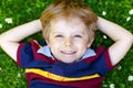 Happy little blond child, kid boy with blue eyes laying on the grass with daisies flowers in the park. Royalty Free Stock Photo