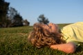 Happy little blond child laying on the grass in the park. Smmer day during school holidays. Amazed kid boy dreaming and Royalty Free Stock Photo