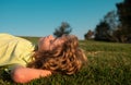 Happy little blond child laying on the grass in the park. Smmer day during school holidays. Amazed kid boy dreaming and Royalty Free Stock Photo