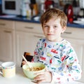 Happy little blond kid boy eating cereals for breakfast or lunch. Healthy eating for children in the morning. Child in Royalty Free Stock Photo