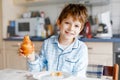 Happy little blond kid boy eating fresh croissant for breakfast or lunch. Healthy eating for children. Child in colorful Royalty Free Stock Photo