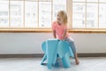 Happy little blonde girl riding on elephant toy in white room Royalty Free Stock Photo