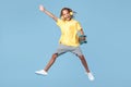 Happy little boy with african dreads with headphone and skateboard jumping over blue background. Royalty Free Stock Photo