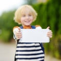 Happy little boy with backpack going to school. Child holding with hands empty white blank card for copy space and free text.
