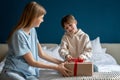 Happy little boy child opening wrapped gift box while celebrating his birthday with mother at home Royalty Free Stock Photo