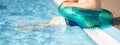 Happy little boy child siting on the edge of the pool with green inflatable ring. Kids legs dipping in the water of the blue