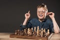 happy little boy in eyeglasses doing idea gesture by finger at table with chess board