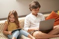 Happy little boy and girl, brother and sister sitting on sofa at home, using laptop and digital tablet and watching Royalty Free Stock Photo