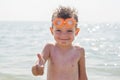 Happy little boy in glasses for swimming shows gesture - thumb up on the background of the sea. Travel and summer vacation concept Royalty Free Stock Photo