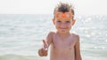 Happy little boy in glasses for swimming shows gesture - thumb up on the background of the sea. Travel and summer vacation concept Royalty Free Stock Photo