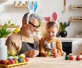 Loving grandfather and child in bunny ear headbands decorating eggs for Easter in light cozy kitchen