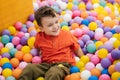 A happy little boy has fun jumping into a dry pool with colorful balls. The kid boy is playing and having a good time in Royalty Free Stock Photo