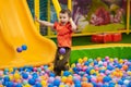 A happy little boy has fun jumping into a dry pool with colorful balls. The kid boy is playing and having a good time in Royalty Free Stock Photo