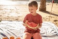 Happy little boy on the picnic beach smiling, eating watermelon, relaxing