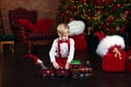 Happy little boy is playing near Christmas tree with toy Xmas train.  Little blond boy in white shirt and red bow tie with suspend Royalty Free Stock Photo