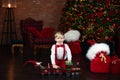 Happy little boy is playing near Christmas tree with toy Xmas train.  Little blond boy in white shirt and red bow tie with suspend Royalty Free Stock Photo