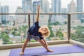 Happy little boy is practicing yoga on his balcony with a panoramic view of the big city Royalty Free Stock Photo