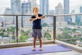 Happy little boy is practicing yoga on his balcony with a panoramic view of the big city Royalty Free Stock Photo